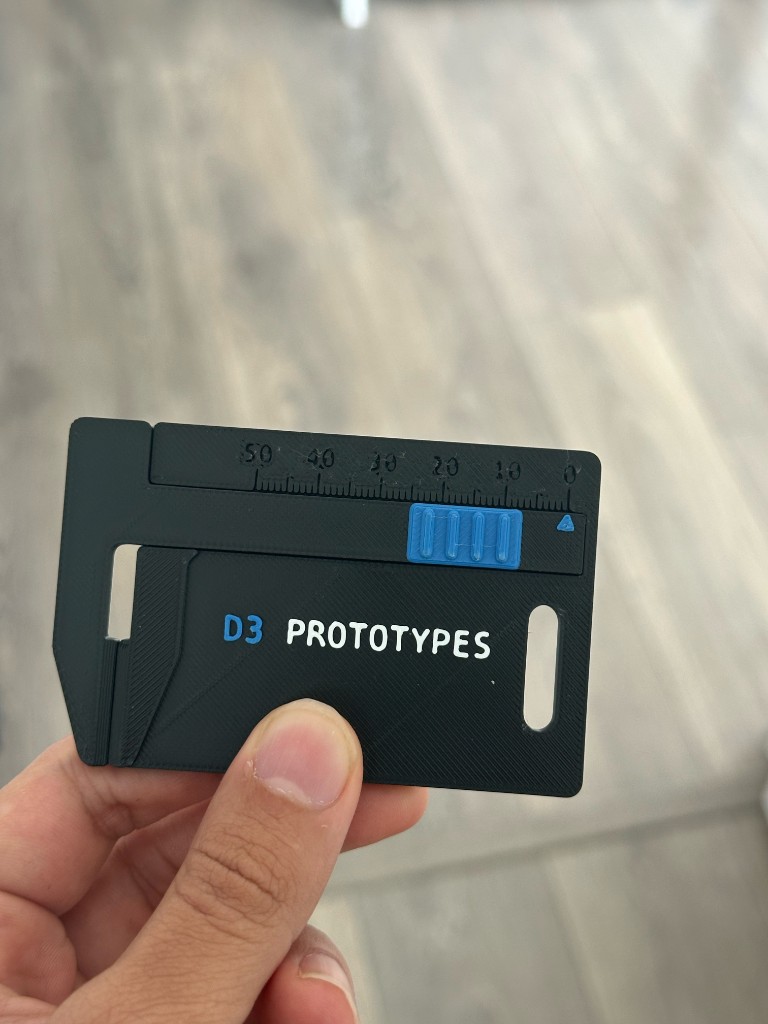 A hand holding a D3Prototypes NFC caliper card with a ruler scale and sliding grip.